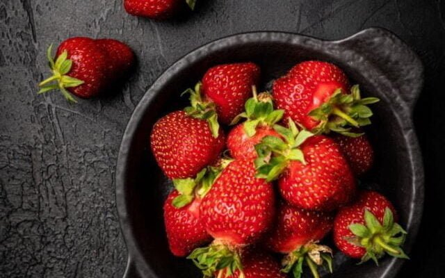 Fresh ripe strawberry in a bowl on dark background, top view, copy space